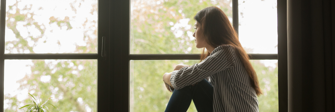 A girl is sitting in a room thinking and looking out of the window.