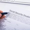 person holding a pen over a form for social security disability claim