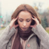 portrait photo of woman outdoors with hands to head or ears looking stressed