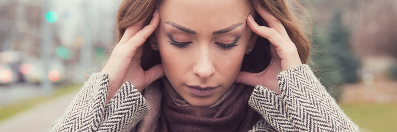 portrait photo of woman outdoors with hands to head or ears looking stressed