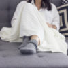 Young woman sitting on sofa covered in blanket, focus on her gray socks