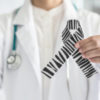 a doctor in their lab coat holding a zebra-striped ribbon for awareness