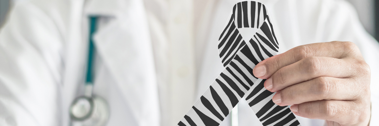 a doctor in their lab coat holding a zebra-striped ribbon for awareness