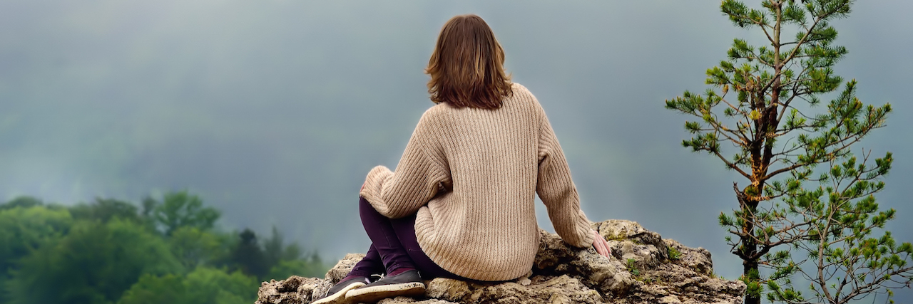 How a Song From 'Next to Normal' Relates to My BPD Recovery A woman sitting on a rock, looking at a mountain, facing away
