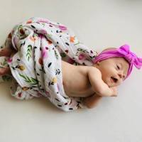 Adorable baby with Down syndrome wrapped in flowery blanket and wearing big pink bow