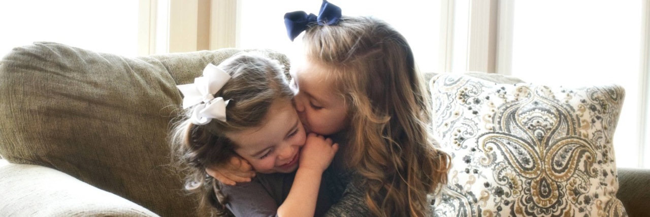 Supporting Siblings of a Child With Cerebral Palsy Jenny's daughters sitting on the couch hugging each other.