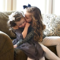 Jenny's daughters sitting on the couch hugging each other.