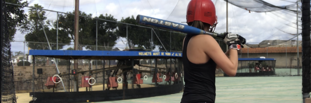 photo of young woman in baseball batting area ready to swing facing away from camera