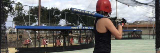 photo of young woman in baseball batting area ready to swing facing away from camera