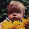 Sarah as a baby, holding a sunflower.