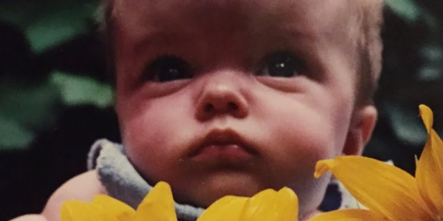 Sarah as a baby, holding a sunflower.