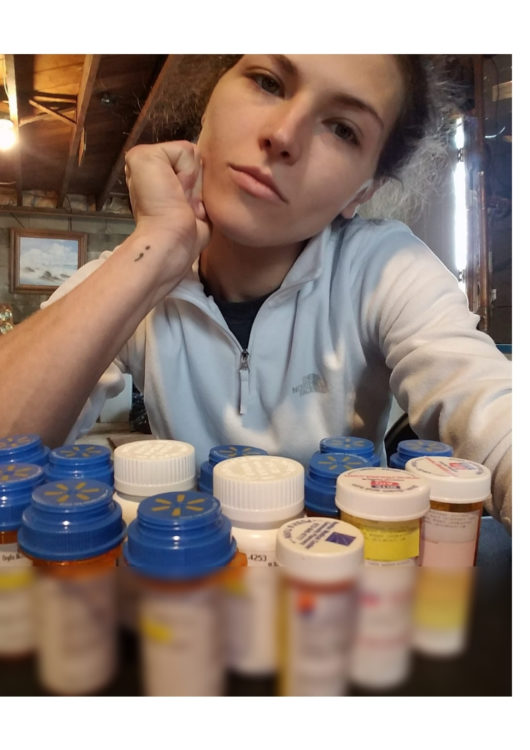A photo of a woman in front of 14 pill bottles, looking straight into the camera. The pill bottle labels are blurred out.
