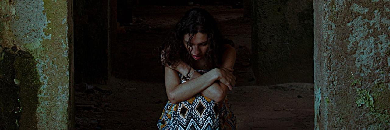 photo of woman on stone floor hugging knees between two stone walls with darkness behind her