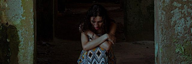 photo of woman on stone floor hugging knees between two stone walls with darkness behind her