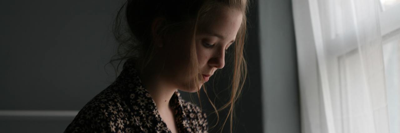 I Wish I Could Talk to My Brother About Our Abusive Childhood photo of blonde woman standing beside window looking sad