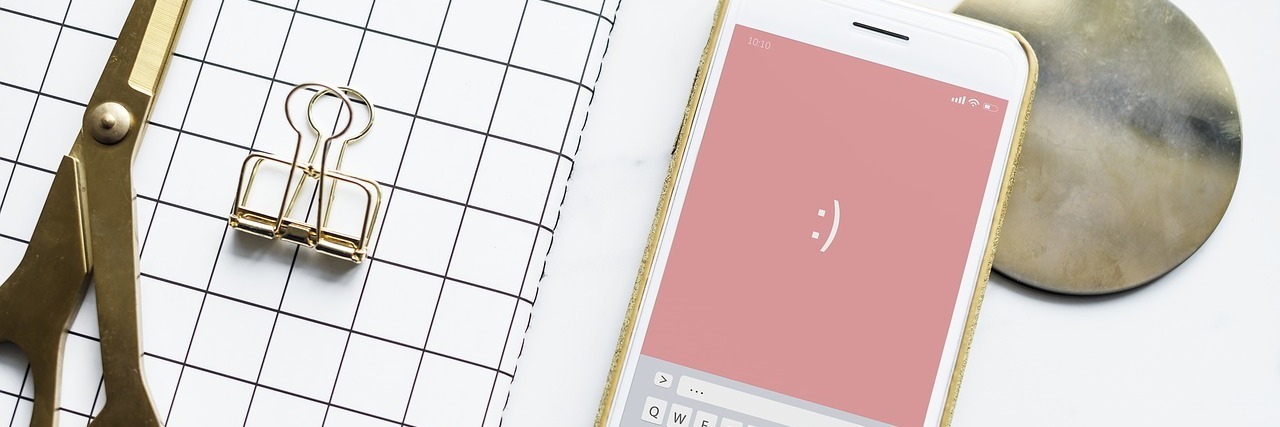 7 Remote Jobs You Can Apply for This March Scissors and clip of a grid pad next to a smartphone with a pink background and smiley face and a coaster