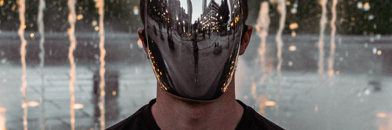photo of man wearing mirror mask with a water jet fountain behind him
