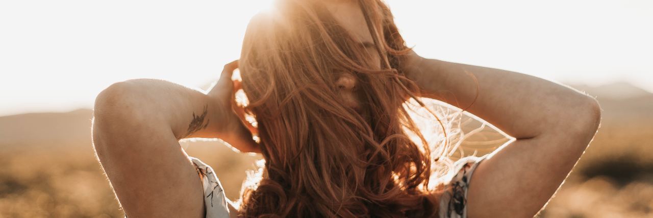 photo of woman with dark blonde hair with hands in hair silhouetted against sun