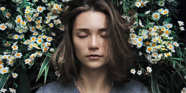 photo of woman with closed eyes standing in front of white flowers