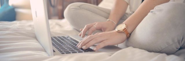 close up photo of woman sitting on bed writing on laptop with screen hidden