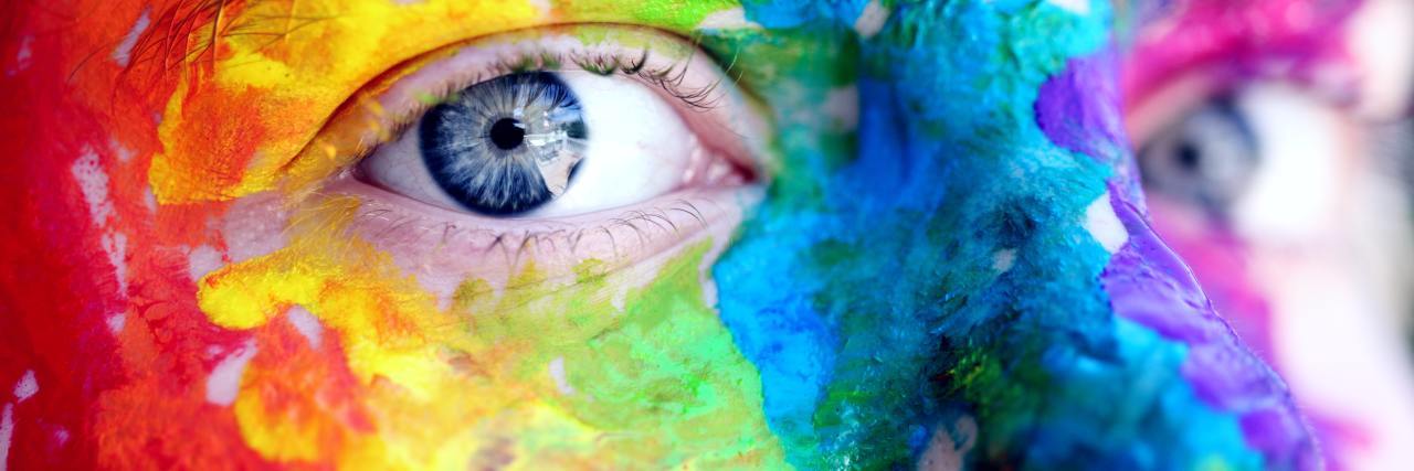 close up photo of person's face and eyes with rainbow face paint