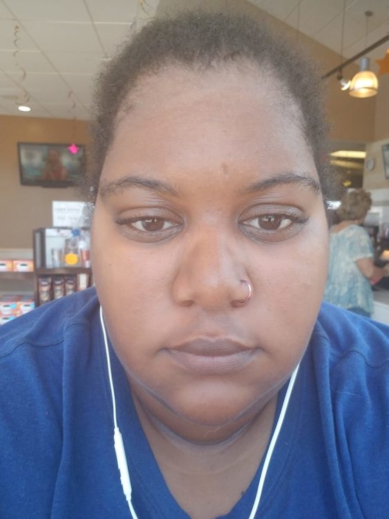 A photo of a young woman sitting in a restaurant with earbuds in, staring into the camera.