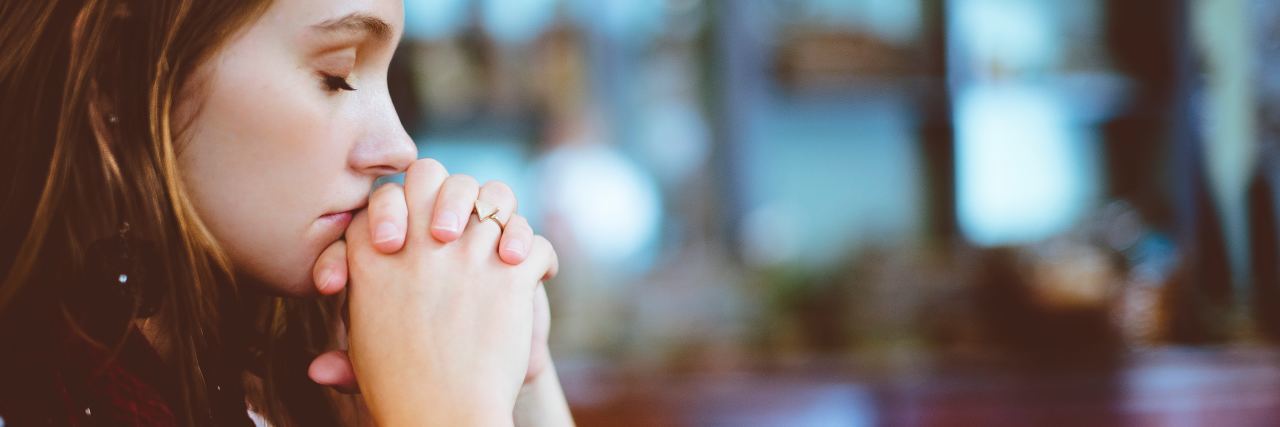Why the Christian Church Needs to Talk About Mental Illness photo of woman praying with church blurred in background