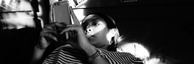 black and white photo of asian woman lying on bed with smartphone
