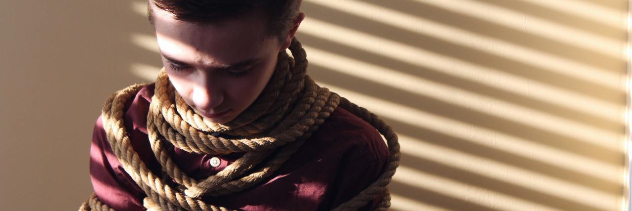 How Bullying Affects Someone's Self-Worth Into Adulthood photo of young boy wrapped in rope and shadow from blinds looking sad