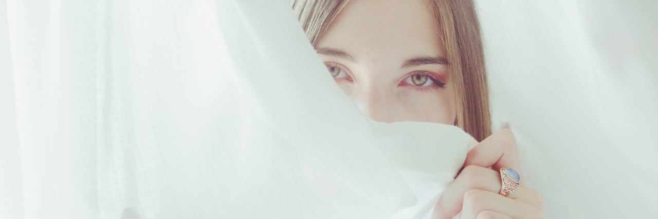 photo of woman partially hiding face with white curtain looking into camera