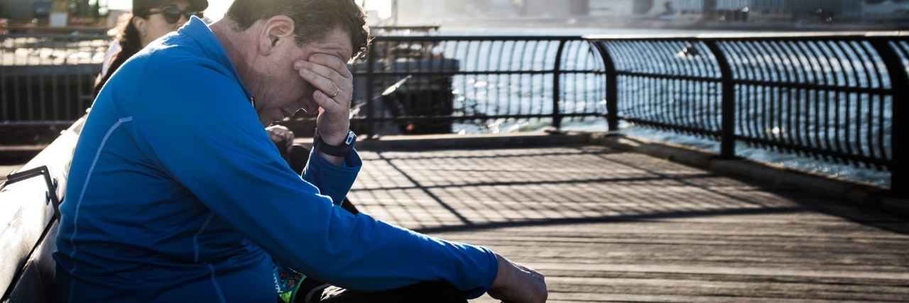 Why Someone Won't Open Up About Depression photo of man with head in hand on boardwalk by river looking depressed