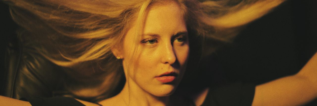 Chronic Migraines and the Pressure to 'Get Better' A woman with blonde hair pulling her hair to the side