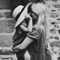 black and white photo of mother holding child close against background of stonework wall