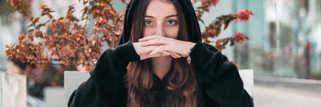 photo of woman looking into camera with hood and hands covering mouth