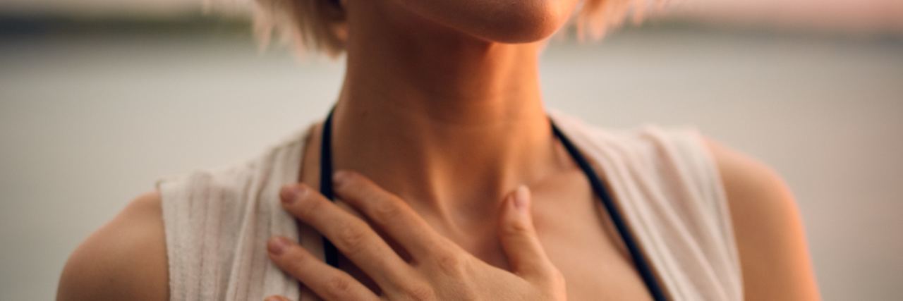 Trying to Accept My 'New Normal' With Crohn's Disease photo of woman with hand on chest and eyes closed at sunset with a slight smile