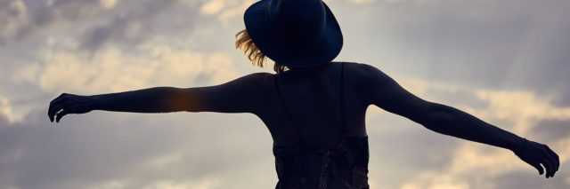 photo of woman in sunlight silhouetted against sunset sky with arms outstretched