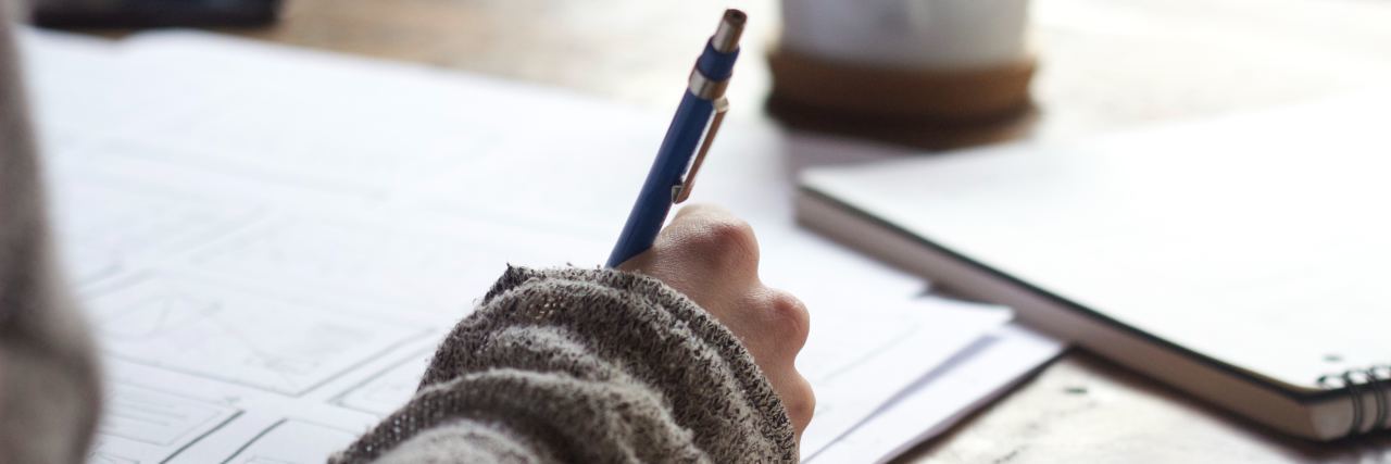 How Anxiety Affects Dream of Being a Writer close up photo of woman's hand holding pen and writing with coffee mug in background