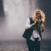 photo of blonde woman standing in front of waterfall partially hiding face