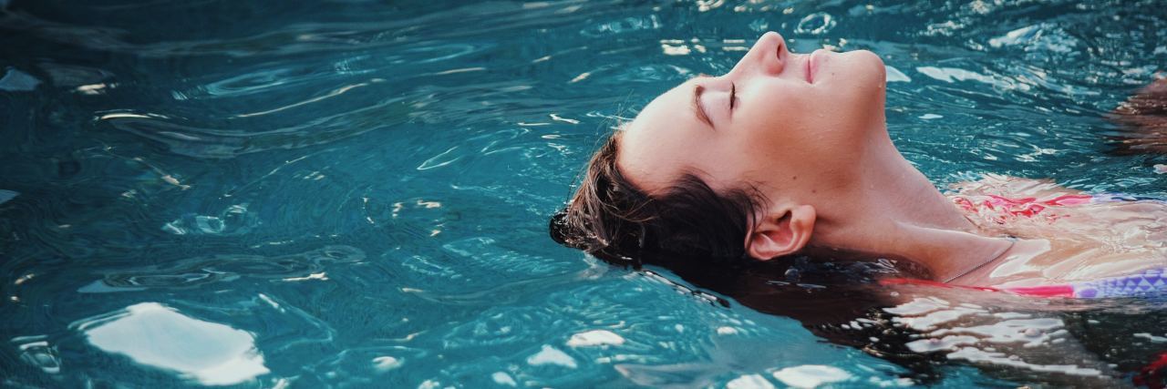 Can Swimming Really Help Your Mental Health? close up photo of woman relaxing in pool with smile on face