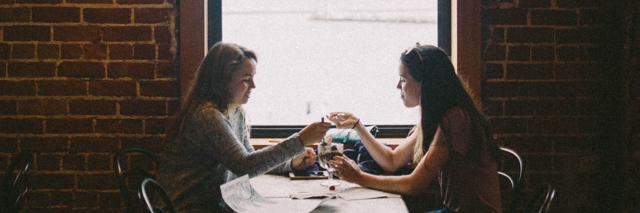 Common Phrases That Hurt People With Eating Disorders photo of two women eating together in front of window and brick wall