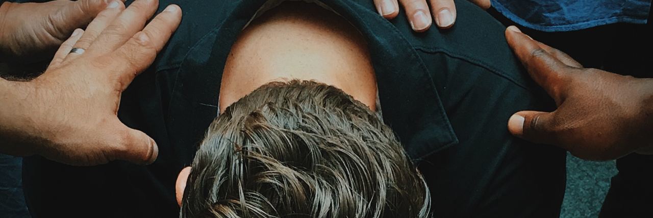 Hope, Mental Health and Suicide close up photo of man hunched over with others touching his shoulders praying