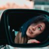 close up photo of woman's reflection in car wing mirror looking up at something above