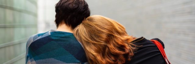 close up photo from behind of two people with one resting their head on the other's shoulder