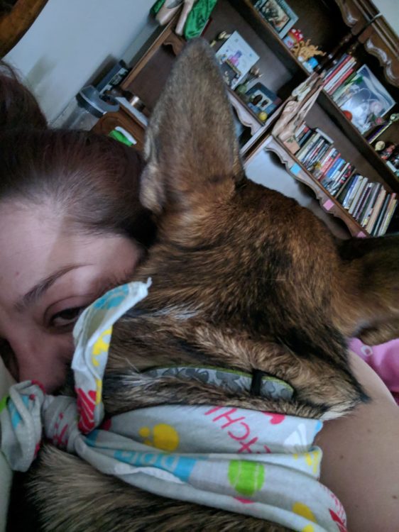A photo of a young woman laying in bed with a dog.