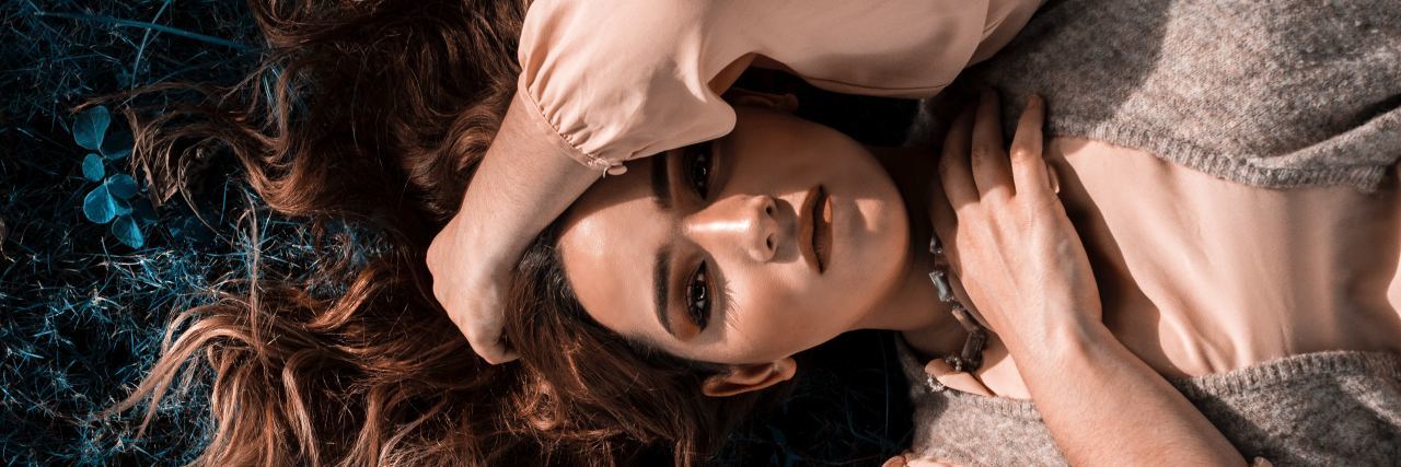 Needing Physical Intimacy With Bipolar and PTSD photo taken overhead of woman lying on ground or grass looking into the camera with longing