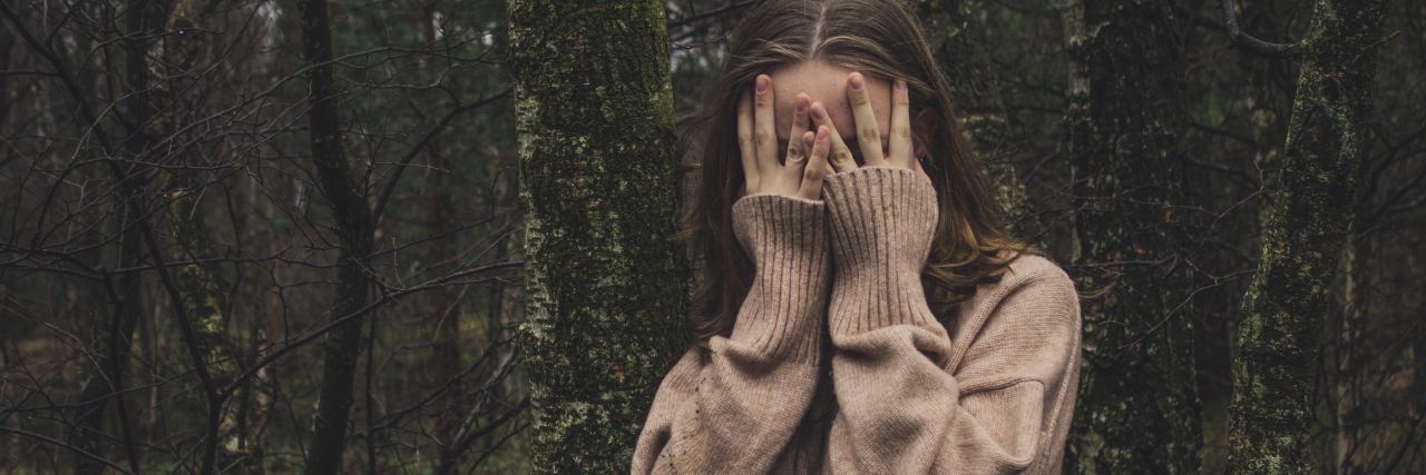 photo of young woman hiding face among trees