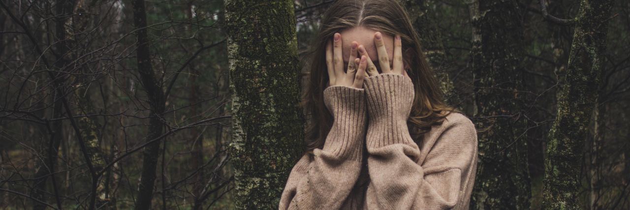 How My Sister Has Been Emotionally Abusive photo of young woman hiding face among trees