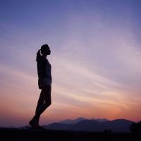 photo of woman standing alone silhouetted against sunset sky