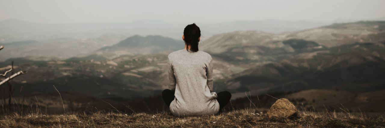 Taking a Break From Advocacy for My Own Mental Health photo of woman with back to camera sitting on stark mountain looking out over valley