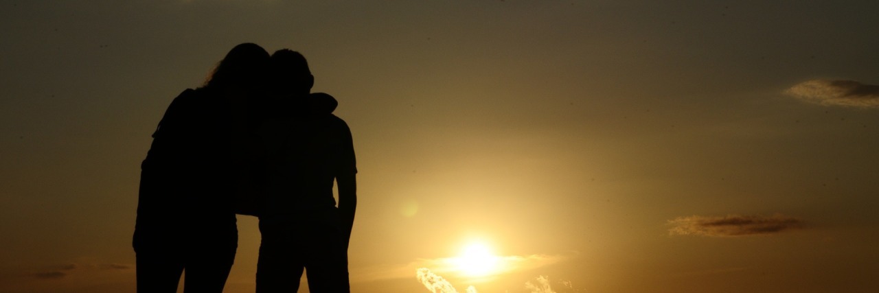 silhouette of mother and son standing close together at sunset
